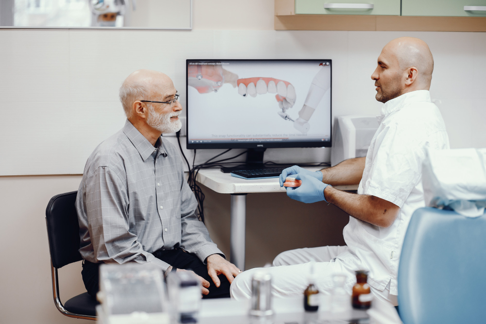 An elderly gentleman consulting with his dentist with a dentistry image on the screen in the background