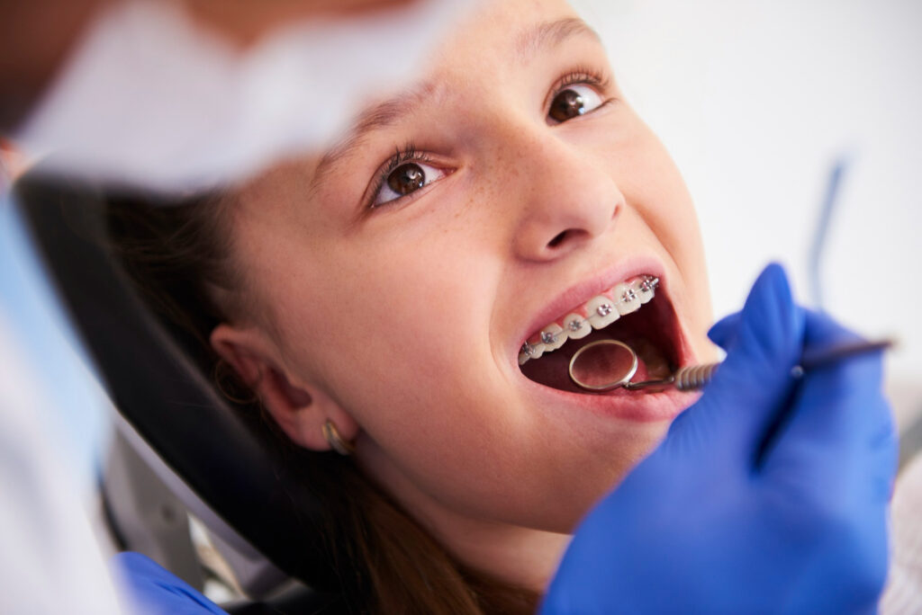 A young woman on a dentist’s chair being inspected for her braces
