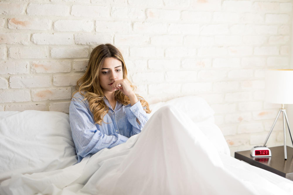 A young woman sitting up in bed in the early morning worrying about something